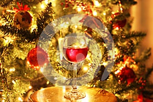 Glass with red wine in front of the night Christmas tree