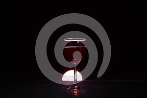 Glass of red wine on glass table with fire around it on black background, romantic photo