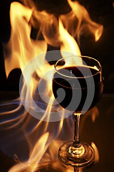 Glass of red wine on glass table with fire around it on black background, romantic photo