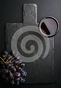 Glass of red wine and grapes on black slate stone board over dark background