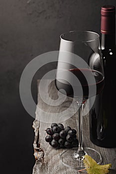 A glass of red wine, grapes and a bottle on an old wooden table