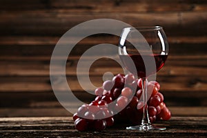 Glass of red wine with grapes on a brown wooden background