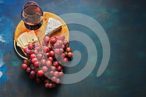 A glass of red wine, grapes, cheese, blue cheese on a cutting board, blue background. Top view, copy space