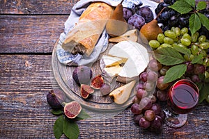 A glass of red wine, grapes, cheese, cork, corkscrew, white bread on a dark background