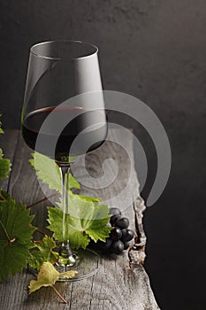 A glass of red wine, grapes and grape leaves on an old wooden table