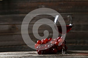 Glass of red wine with grapes on the grey wooden background