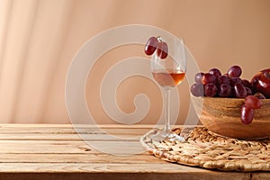 Glass of red wine and grapes on wooden table over beige background. Wine tasting concept