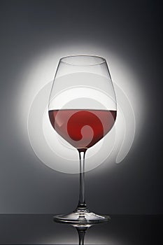 Glass with red wine on a gray background with backlight and reflection