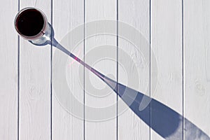 A glass of red wine and its long shadow on a white plank background. Top view. Copy space