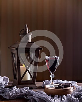 Glass with red wine. Near broken chocolate. Lantern with a candle in the background