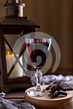 Glass with red wine. Near broken chocolate. Lantern with a candle in the background