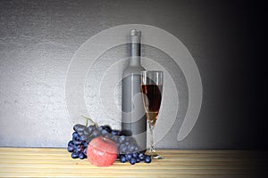 Glass of red wine near wine bottle next to apple and bunch of grapes