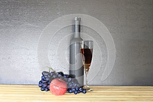 Glass of red wine near wine bottle next to apple and bunch of grapes