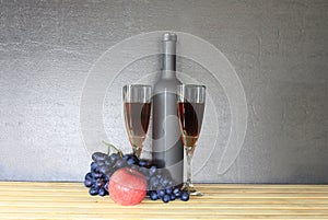 Glass of red wine near wine bottle next to apple and bunch of grapes