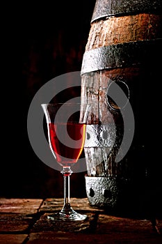 A glass of red wine next to an oak cask