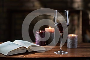 Glass of red wine, open book with candles in the background on wooden table