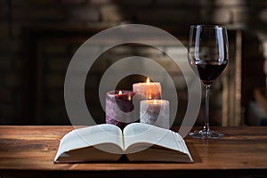 Glass of red wine, open book with candles in the background on wooden table
