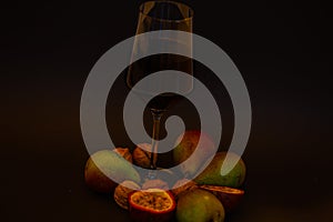 Glass of red wine with passion fruit, walnut and pear, black background