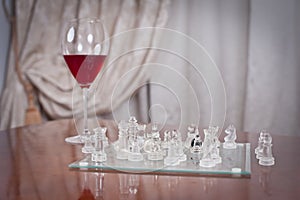 Glass with red wine and pieces on the chessboard. Set of chess figures on the playing board near a glass with red win