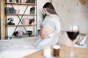 A glass of red wine and pills on the background of a pregnant woman. Alcoholic concept.