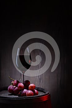 Glass of red wine and pink grapes on wooden barrel