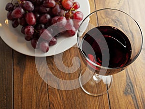 Glass of red wine and plate with white grapes.