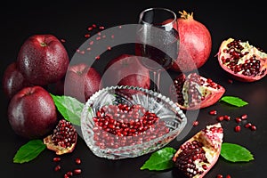 Glass red wine, pomegranates, apples, green leaves on black background
