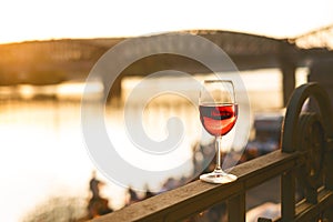 Glass of red wine on a railing with sunset in a Prague city. Concept of free time in the city and drinking alcohol.