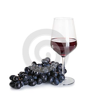 Glass of red wine with ripe grapes on white background