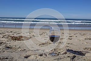 Glass of red wine on the sand on the beach overlooking the sea in a romantic atmosphere