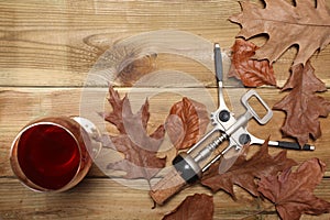 Glass of red wine, cork and some death leaves rest on a wooden table