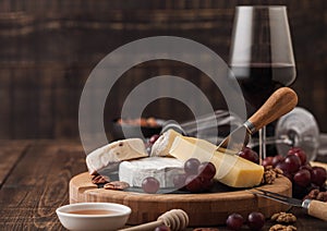 Glass of red wine with selection of various cheese on the board and grapes on wooden background. Blue Stilton, Red Leicester and