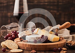 Glass of red wine with selection of various cheese on the board and grapes on wooden background. Blue Stilton, Red Leicester and