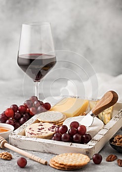 Glass of red wine with selection of various cheese in wooden box and grapes on light table background. Blue Stilton, Red Leicester