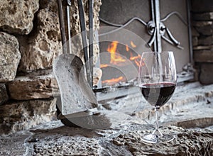 Glass of red wine sitting on the hearth in front of fire place.