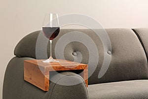 Glass of red wine on sofa with wooden armrest table in room, space for text. Interior element