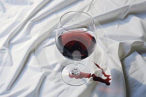 Glass of red wine spilled on a white tablecloth or sheet. AI generated