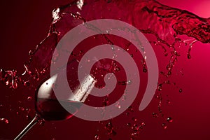 Glass and red wine splash on a dark red background