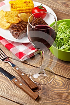 Glass of red wine, steak with grilled potato, corn and salad