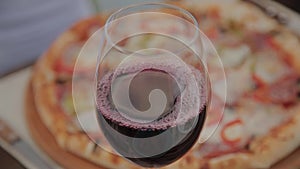 A glass of red wine on the table against the background of fresh pizza.