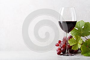 A glass of red wine on the table, grapes and grape leaves. Light background