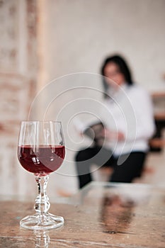 A glass of red wine takes center stage, with a woman reading a book in the background