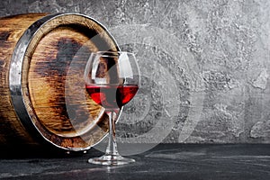 Glass with red wine for tasting and wooden barrel in dark cellar