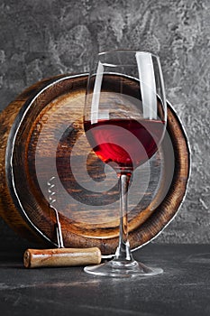 Glass with red wine for tasting and wooden barrel in dark cellar