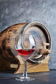 Glass with red wine for tasting and wooden barrel in dark cellar