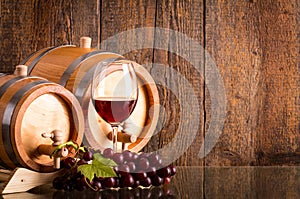 Glass of red wine with two barrels and grapes