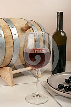 A glass of red wine with a wooden barrel and bottle