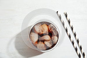 Glass of refreshing cola with ice cubes on white wooden background