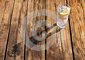 Glass of refreshing drink with ice and lemon for hot summer day on wooden table