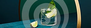 Glass with refreshing drink with mint, ice and lime slice on wooden surface